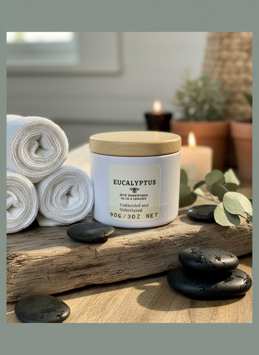 Eucalyptus candle on a wooden surface with towels, candles, and stones in the background
