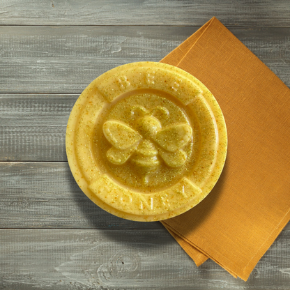 Soap medallion with a bee design on top, placed on a wooden surface with an orange napkin.