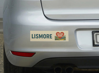 Bumper sticker on a car reading 'Lismore You Are Here' with a scenic design.