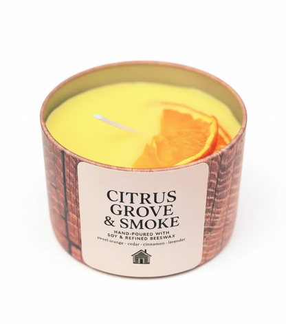Candle labeled 'Citrus Grove & Smoke' with sliced oranges on a wooden surface