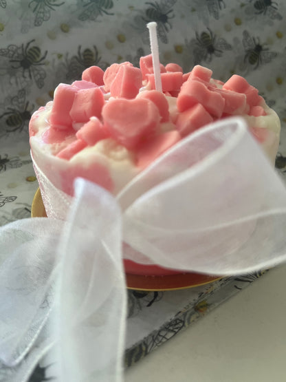 Pink heart-shaped candles on a cake with a white ribbon, against a patterned background.