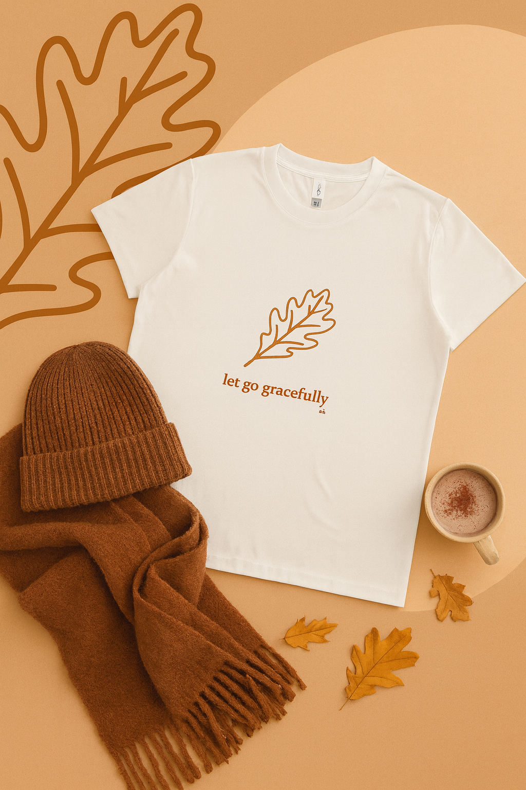 White t-shirt with leaf design and 'let go gracefully' text on a brown background with accessories.
