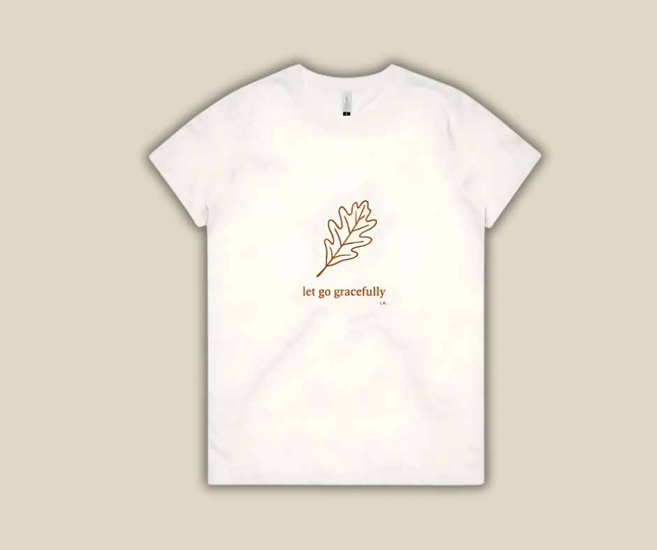 White t-shirt with a leaf design and text 'let go gracefully' on a beige background