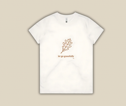 White t-shirt with a leaf design and text 'let go gracefully' on a beige background
