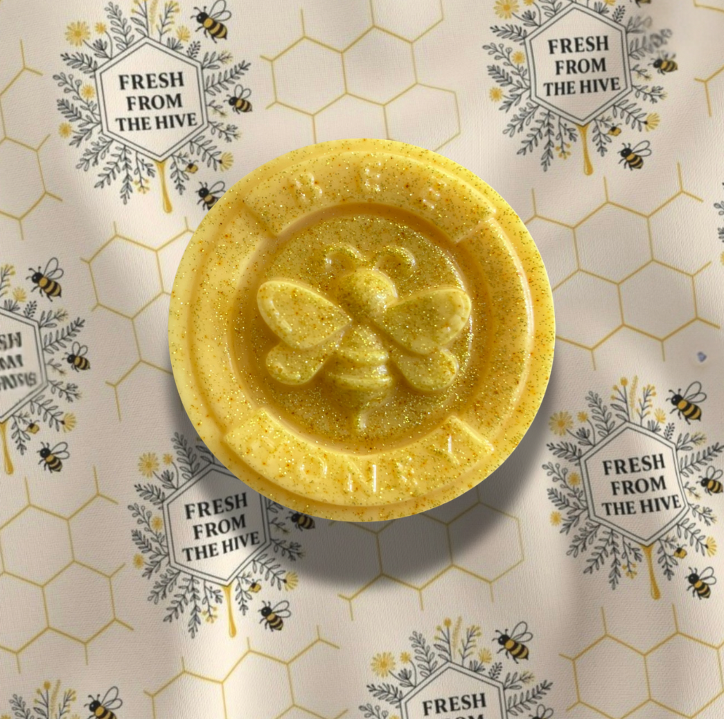 Yellow bee-themed soap medallion on a patterned background with honeycomb and bee designs.