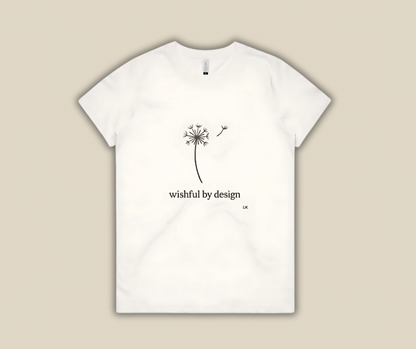 White t-shirt with a dandelion design and 'wishful by design' text on a beige background